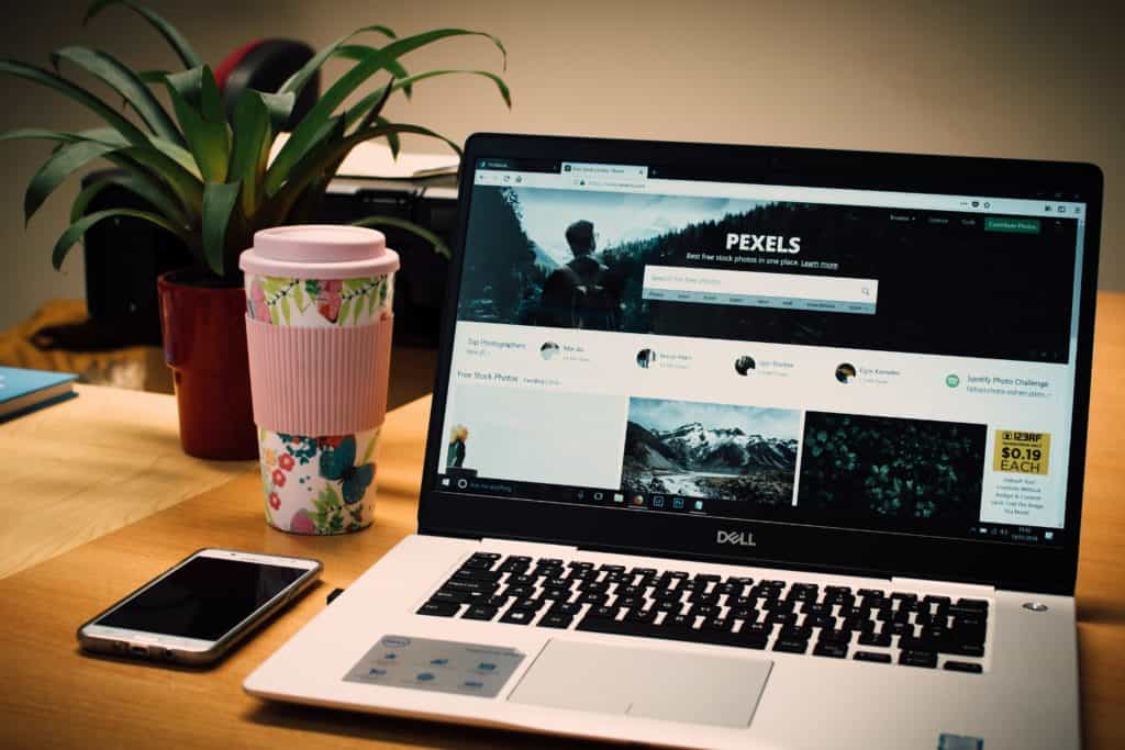 Dell laptop with a tumbler cup and a mobile phone beside it